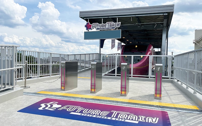 改札ゲートの先に、車両の入口と「FUTURE TRAIN」のサインが見える高架上の店舗