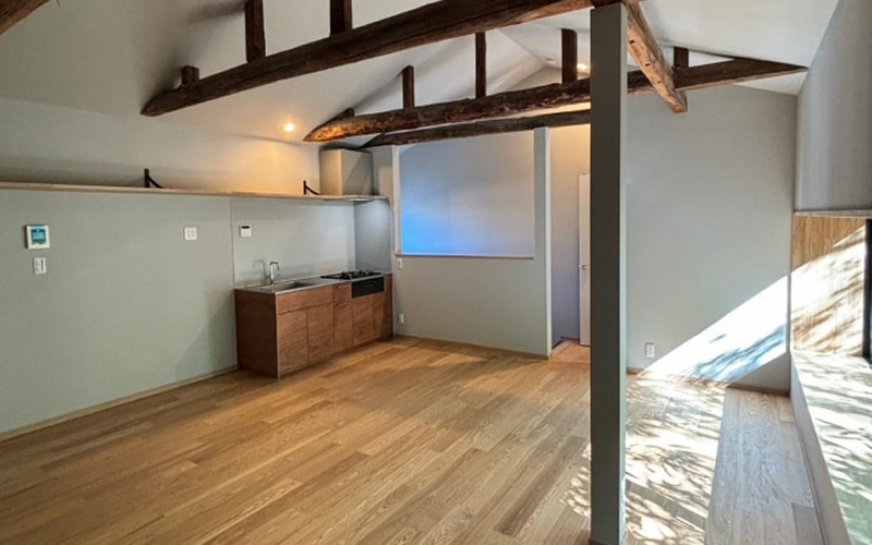 梁を見せた勾配天井の下に、無垢の床とキッチンが広がる住戸